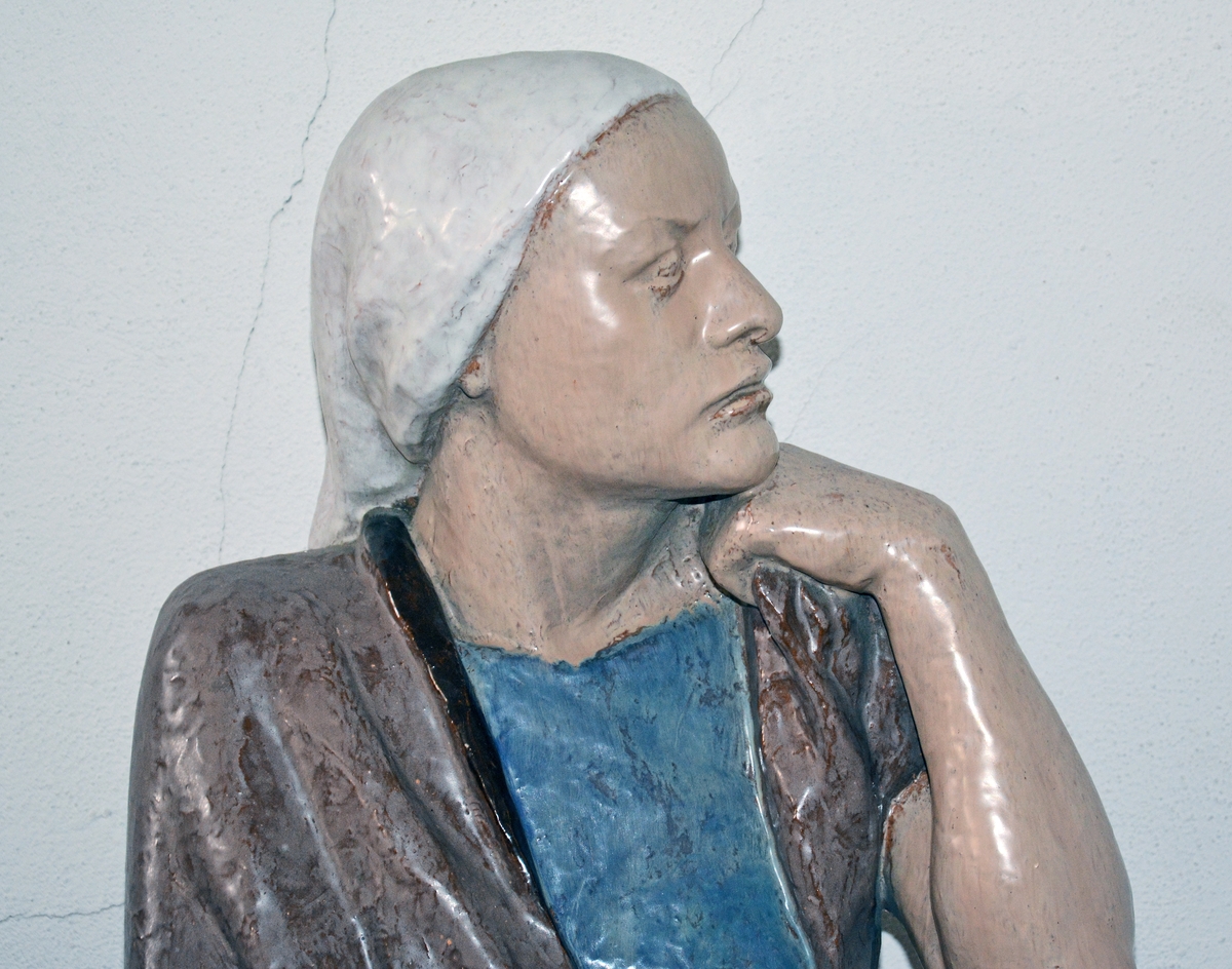 Maria-figur - står på gulvet, ser mot krusifikset på veggen.