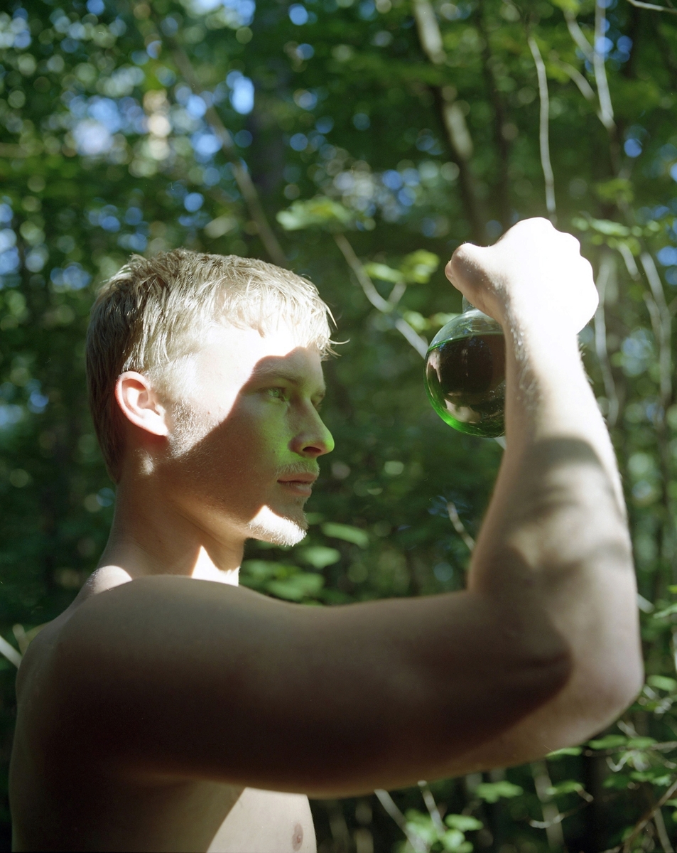 Fotografiet viser en ung mann som betrakter flytende grønn veske fra et reagensglass ute i et landskap.