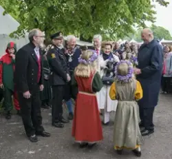Kongeparet tas imot av avdelingsdirektør ved Anno Domkirkeodden, Magne Rugsveen, iført Gudbrandsdalsbunad. Kongeparet mottar blomster fra to blomsterpiker i middelalderkjoler, med blomsterkrans på hodet.