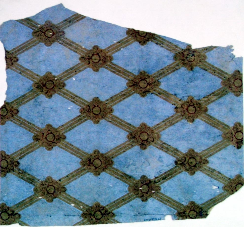 Ett litet snedrutmönster med kryssornament i ljusblått och vinrött på ofärgat papper.