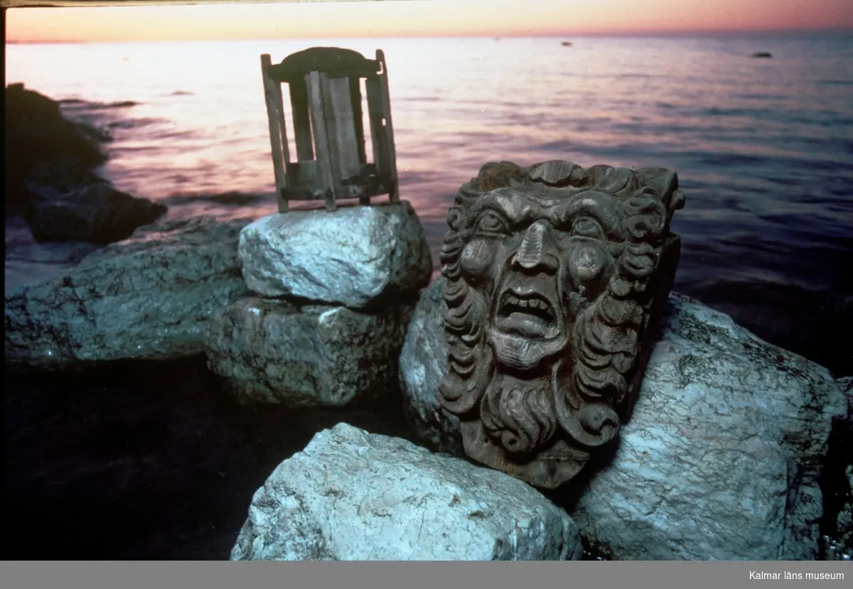 Skulptur och lykta vid strand i solnedgång.