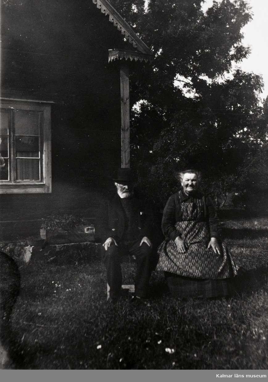 Kalle Bäck med hustru sittande vid stugknuten.