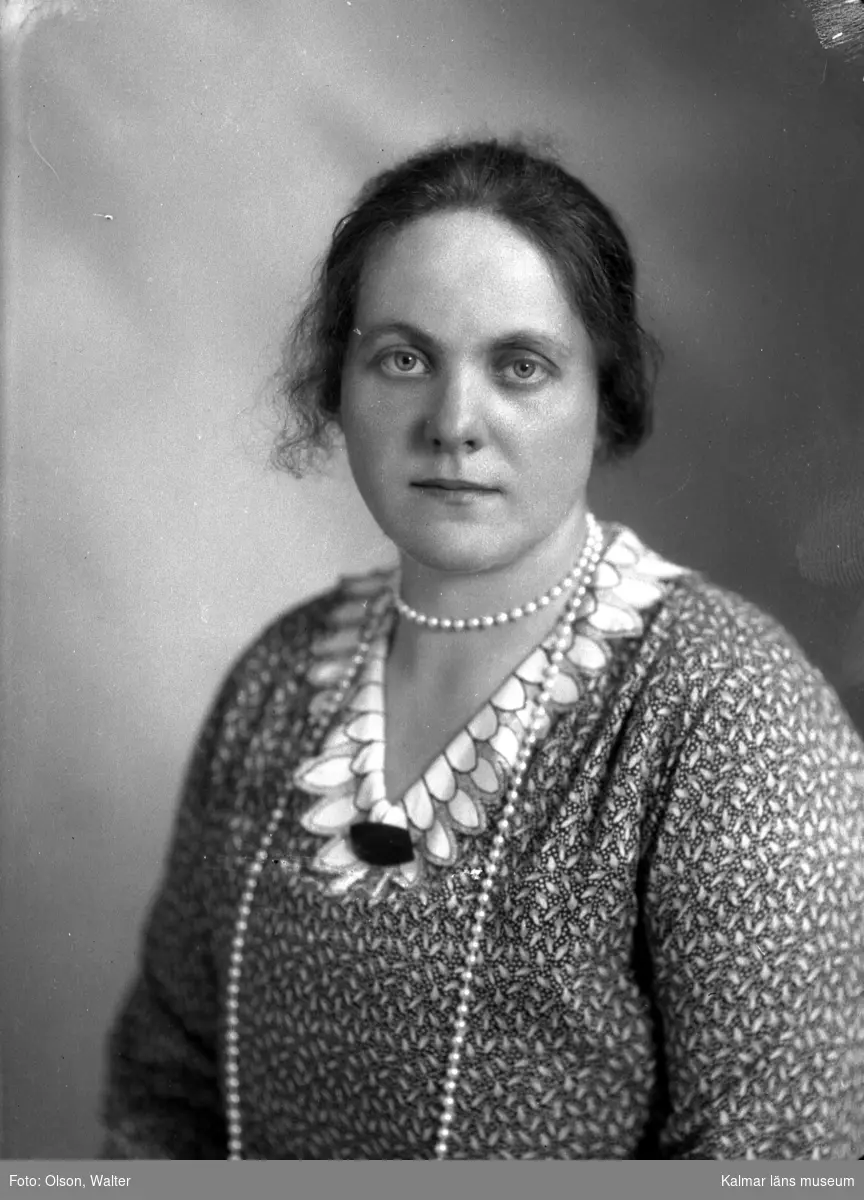 Ateljébild på en kvinna i halsband och brosch. Enligt Walter Olsons journal är bilden beställd av fru Gottfrid Johansson.