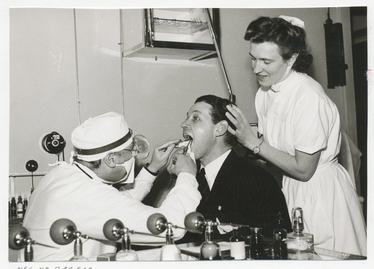 En man hos tandläkaren och en tandsköterska som stöttar.