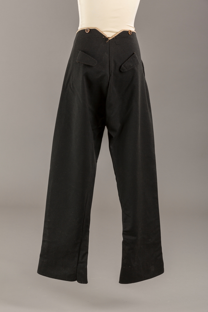 Form: Bena utvidet nederst. Lerretskant rundt livet, spensel i ryggen, mangler spenne i sepnsel?
Delvis foret. To lommer. 5 knapper, mangler en knapp.