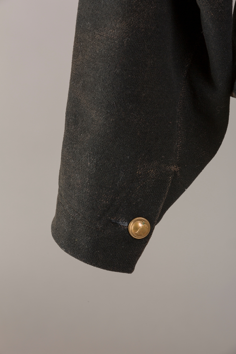 Form: Enkeltspent.

Foret med lin. Forsterket med silke på et lite stykke på ryggen. 12 messingknapper med mønster og tallet 1. Hempe i lin. Bendelbånd med knappehull.