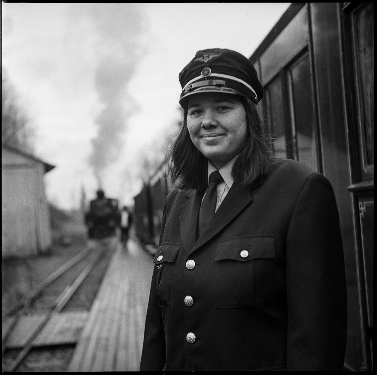 Kvinnelig uniformert frivillig i tjeneste på Bingsfos stasjon. I bakgrunnen skimtes lokstallen på Bingsfos og et damplokomotiv.