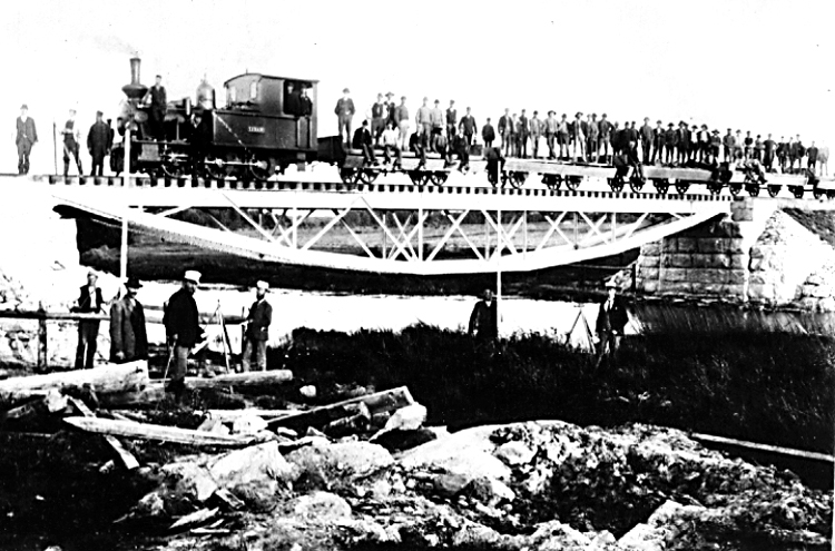 Kålltorp.
Järnvägsbron över Flian  vid Kålltorp, vid V.G.J.:s bygge år 1899.
"Fotot visar hur man vid banbygget år 1899 "provtrycker" bron över Flian vid Kålltorp. 
Troligen är det beställt av bolagsledningen, eftersom byggnadschefen, sedermera järnvägens VD, står på parad med sin bekanta käpp i förgrunden. Lokförare är A.G. Eldh, sedermera lokmästare vid LSSJ."

Ivar Mjörnfors, Kristianstad, har i brev 5.11.1966 meddelat  vidstående text om fotot.