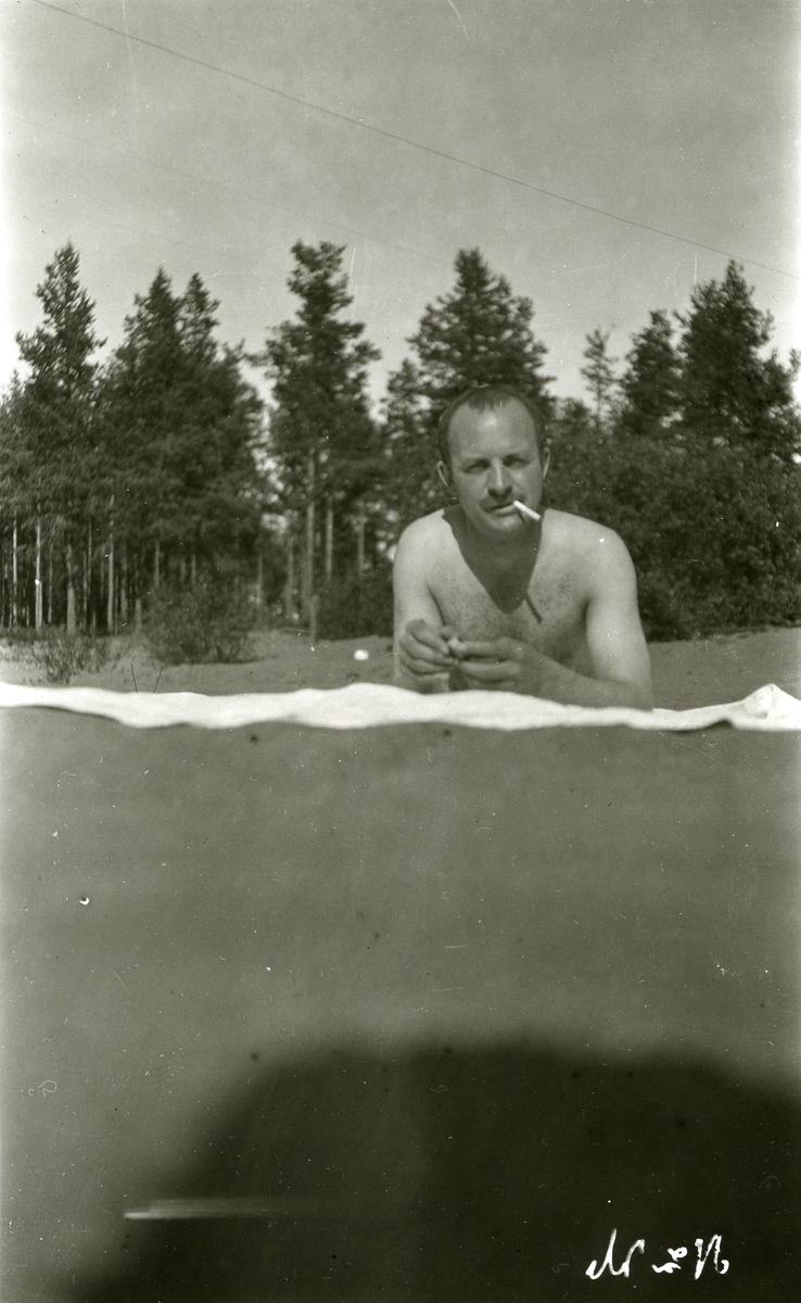 Haakon Garaasen (6/7 1887 - 1957) liggende på teppe i sola med sigarett i munnviken, ved Siljan, Sverige.