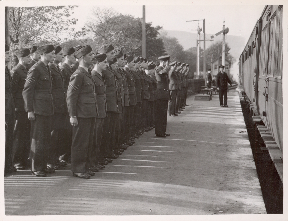 Soldater oppstilt på jernbaneperrong. Tog til høyre.