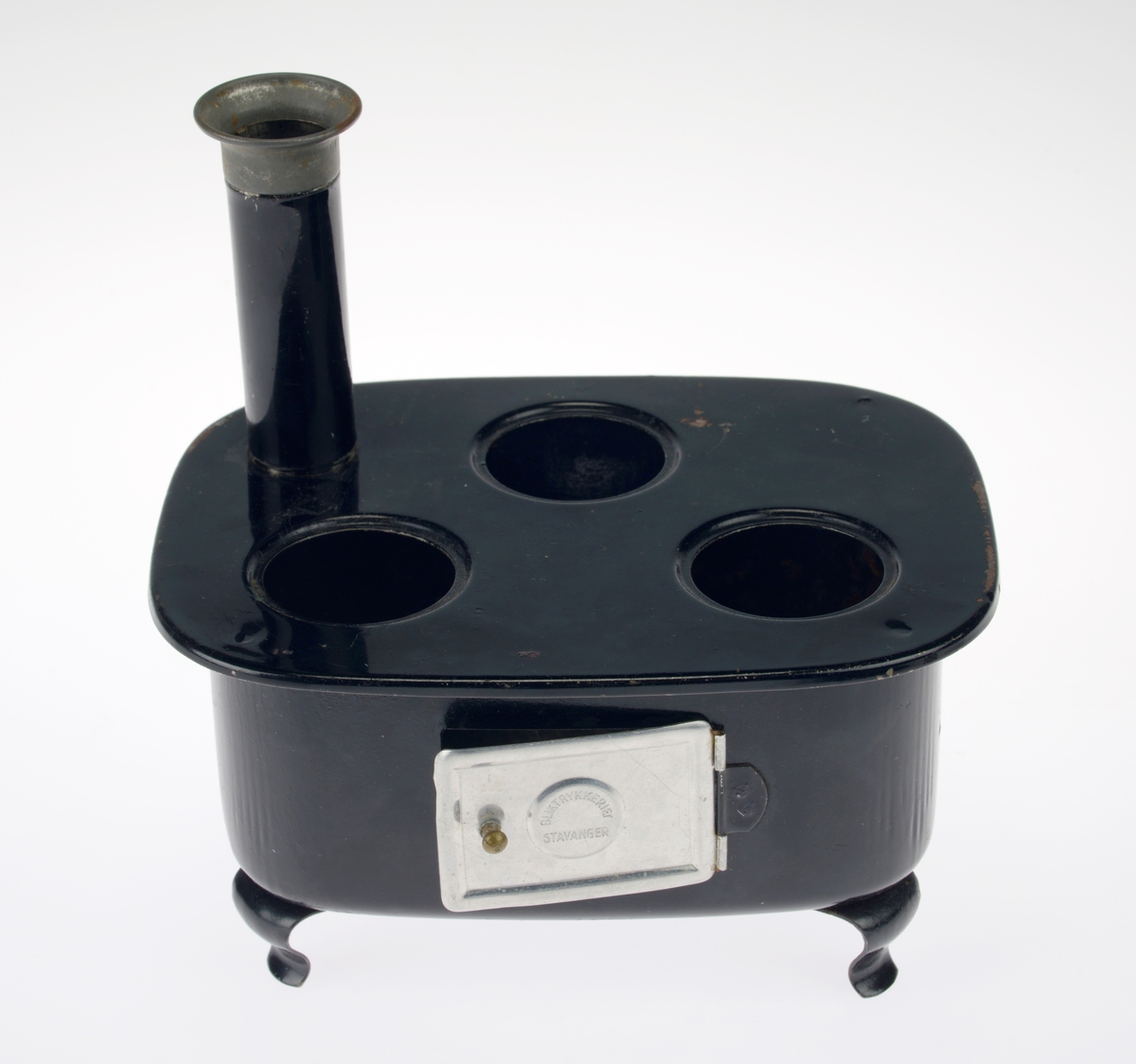 En liten komfyr med tre kasseroller og en steikepanne. Gjenstandene er undernummerert 01-05.
FTT.54454.01: En svartlakkert lekekomfyr som er firkantet med avrundede hjørner. Den er trolig laget av jernblikk og blikk. På kokeflaten er det tre hull for å plassere kasserollene på. Bakerst til venstre er det en 8cm høy pipe. I front er det en sølvfarget blikkdør som er festet med hengsler. På døren er det innskrift og et lite messingfarget og rundt håndtak. Komfyren har buede bein.
FTT.54454.02: En høy kasserolle laget av blikk. I hver side er det loddet på håndtak. 
FTT.54454.03: En lav kasserolle laget av blikk. I hver side er det loddet på håndtak.
FTT.54454.04: En lav kasserolle laget av blikk. Det har vært festet et langt håndtak i den ene siden, men det er nå løs.
FTT.54454.05: En steikepanne laget aav blikk. Håndtaket mangler.