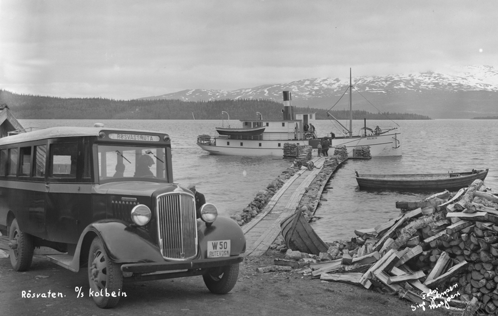 Dampskipet D/S Kolbein ved kai i Bjørkåsen, Røssvatnet. Det gikk i rutetrafikk på Røssvatnet i Hattfjelldal i perioden 1915-1945.
På bildet ligger båten ved kai i Bjørkåsen og vi ser Røssvassholmen i bakgrunnen.
Vi ser at lokalbussen korresponderer med rutebåten, i bussbasen til Rutebilhistorisk Forening er buss med reg. nr W-50 oppført som en 1935-modell Reo tilhørende Karl Othar Helmersen (1897-1991) Hattfjelldal (Røsvassruta).
Båten var vedfyrt, vi ser vedstabler både på kaia og i forgrunnen. Lokalbussen står og venter.