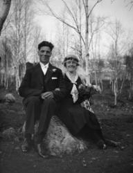 Brudepar, sitter på en stein i en bjørkelund