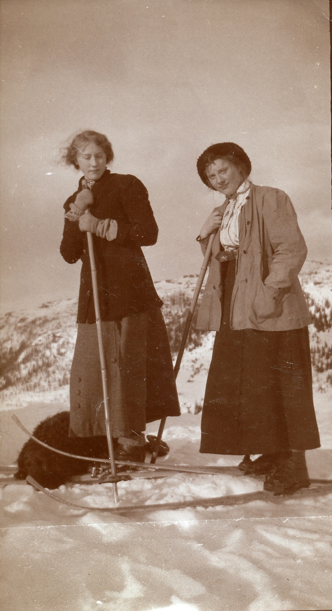 To unge jenter på ski: skjørt, en stav med trinse.