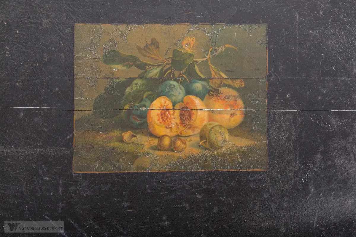 Et stilleben sentralt på bordplaten av en klase med plommer, to fersken, den ene brutt åpen, to nøtter og en fiken.