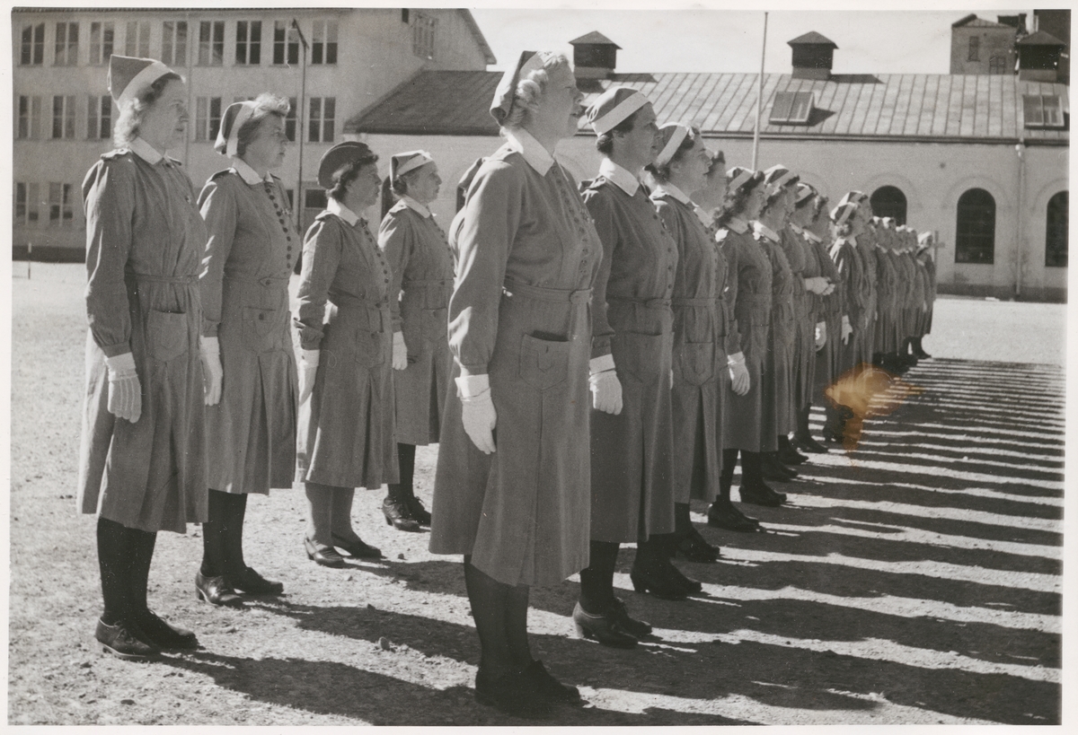 Uniformsklädda kvinnor från lottakåren står uppställda i två rader inne på Bataljon Sparres innegård.
