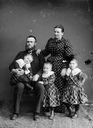 Gruppebilde av en familie. Far, mor og tre små barn. Far sit