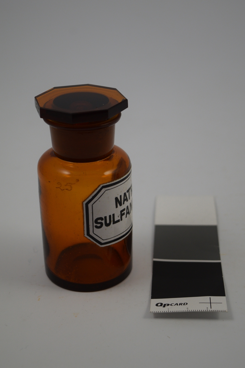 Brun glasskrukke med brun propp. Påført etikett, hvit med svart skrift. Har inneholdt Natrii sulfanilas, et sulfatpreparat - mot mikroorganismer.