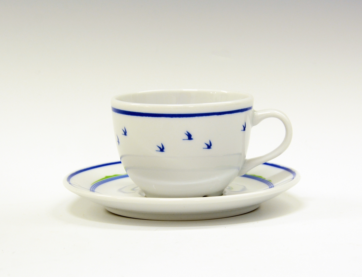 Kopp av porselen med hvit glasur. Dekorert med blå strek og blå flyvende fuglesilhuetter.
Modell: Roma