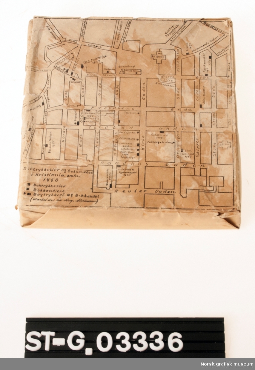 En innpakket klisje med motivet trykt på utsiden. Motivet viser et kart over boktrykkerier og bokhandlere i Kristiania omkring 1850.