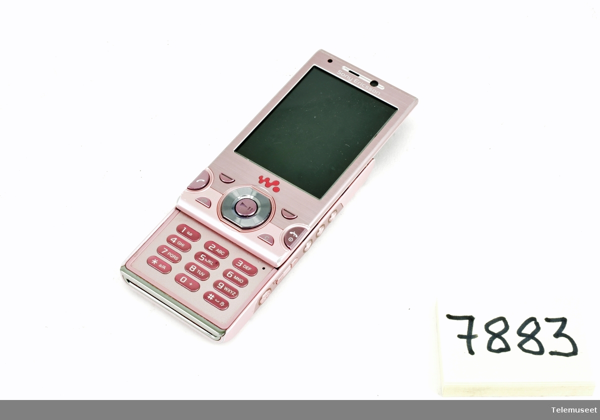 Rosa mobiltelefon med tilhørende utstyr som: lader, minnepinne, datakabel, informasjons brosjyrer og fire gummi ørebeskyttere til hodetelefon. Batteri, Netcom simkort og 8GB minnebrikke medfølger. Mangler hodetelefoner, bruksanvisning og mulig et nakkebånd.