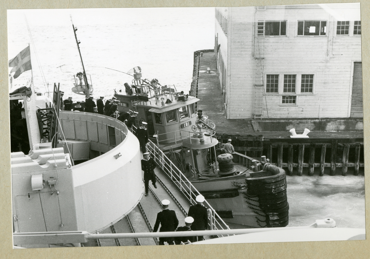Bilden föreställer en bogserbåt klämd mellan en kajkonstruktion och minfartyget Älvsnabben. På Älvsnabbens däck syns uniformsklädda besättningsmän. Bilden är tagen under minfartygets långresa 1966-1967.