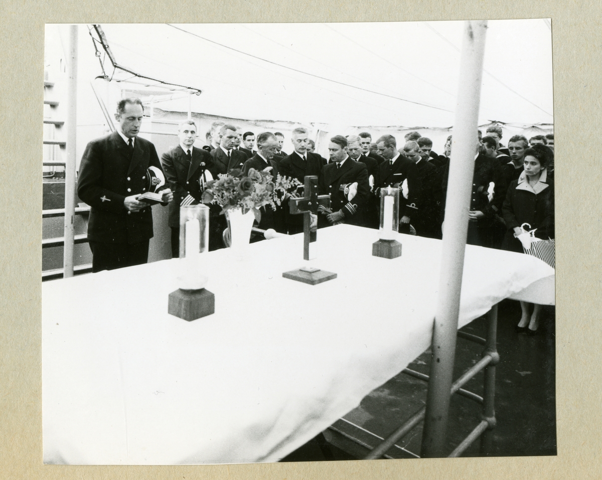 Bilden föreställer högbåtsman Grundströms minnesgudstjänst ombord på minfartyget Älvsnabben. På bilden syns ett altare med ljus, blommor och ett kors. Bakom altaret står besättningen klädda i mörka uniformer med huvudbonaderna under armarna medan prästen talar. Bilden är tagen under Älvsnabbens långresa 1966-1967.
