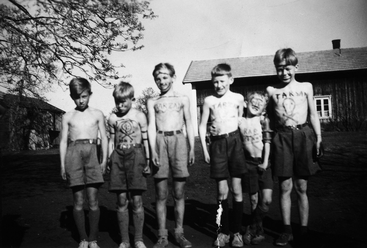 Gruppe 6 gutter,Skøyen gård, Løten. "Tarzan", dødningehode malt på brystkassa. Fra venstre: Even Hansen, Jon Reistad, Nils Arne ("Skipp") Spangen, Tor Ingvoldstad, Helge Reistad. Navnet på gutten til høyre er ukjent.