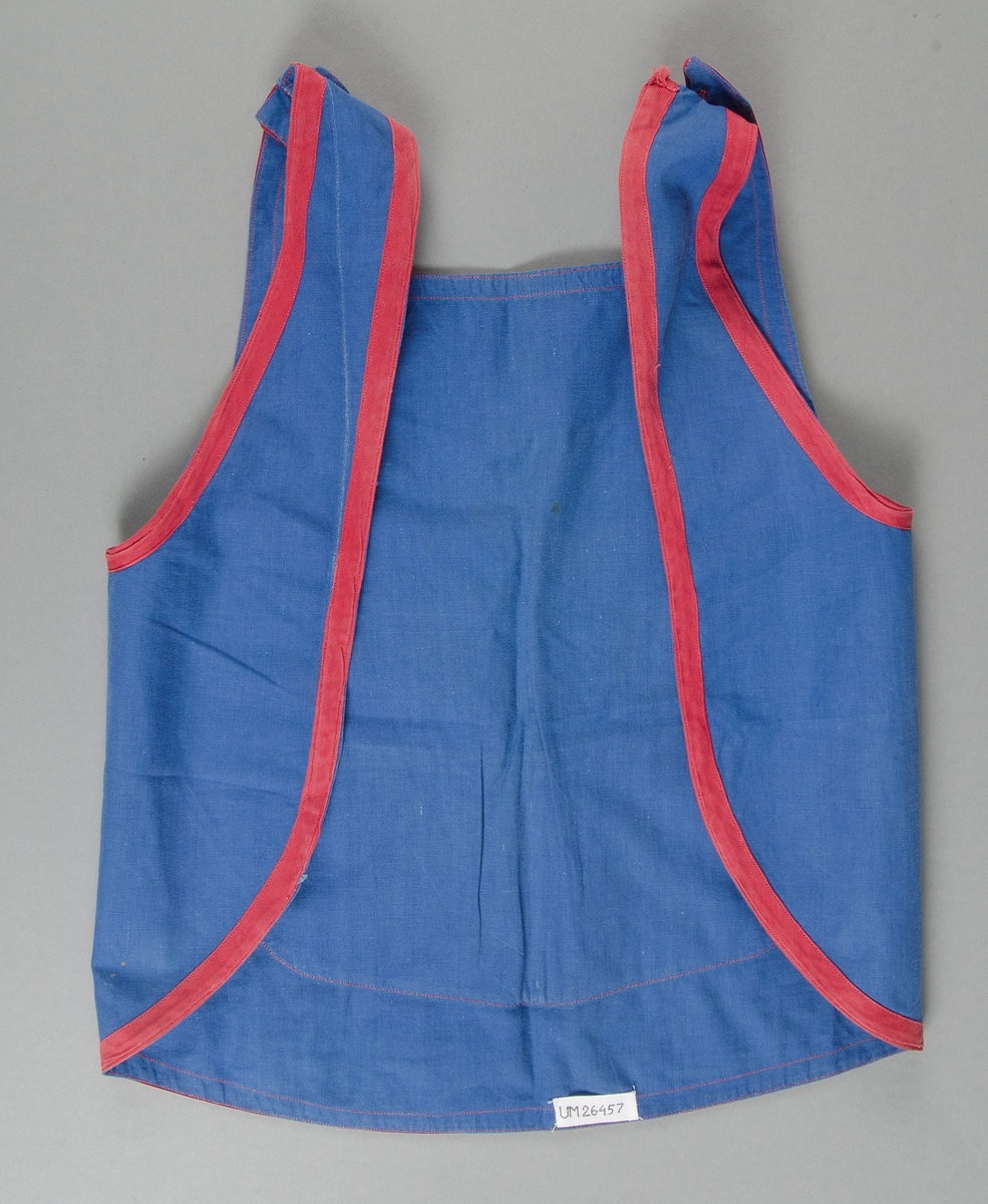 Förkläde för barn av blå bomullslärft kantat med röda band, sytt i ett stycke med rundad nederkant, bröstlapp och axelband som knäpps med röd knapp på axlarna. Bred ficka på magen.
