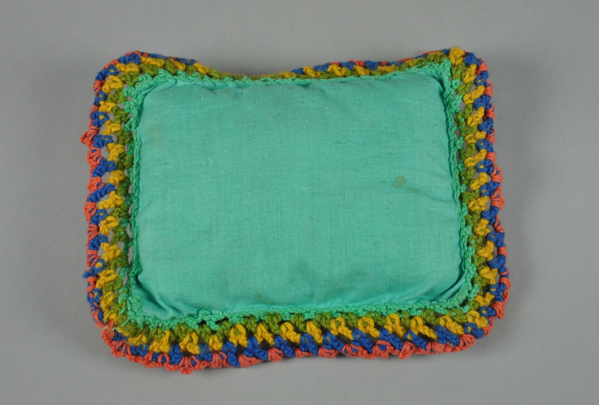 Liten pute til dukkeseng, med brodert prydsøm. Puten har grønn tekstil med brodert prydsøm i gule, blå og røde farger.