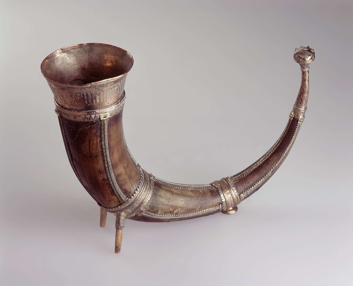 Drikkehorn med metallbeslag rundt kanten, to ringer rundt hornet, et beslag på spissen og smale langsgående beslag. Den største ringen har fester for støttebein. De nåværende beina er ikke de opprinnelige. Beslagene er av forgylt bronse. Krone i spissen. Graverte beslag med geometriske border.