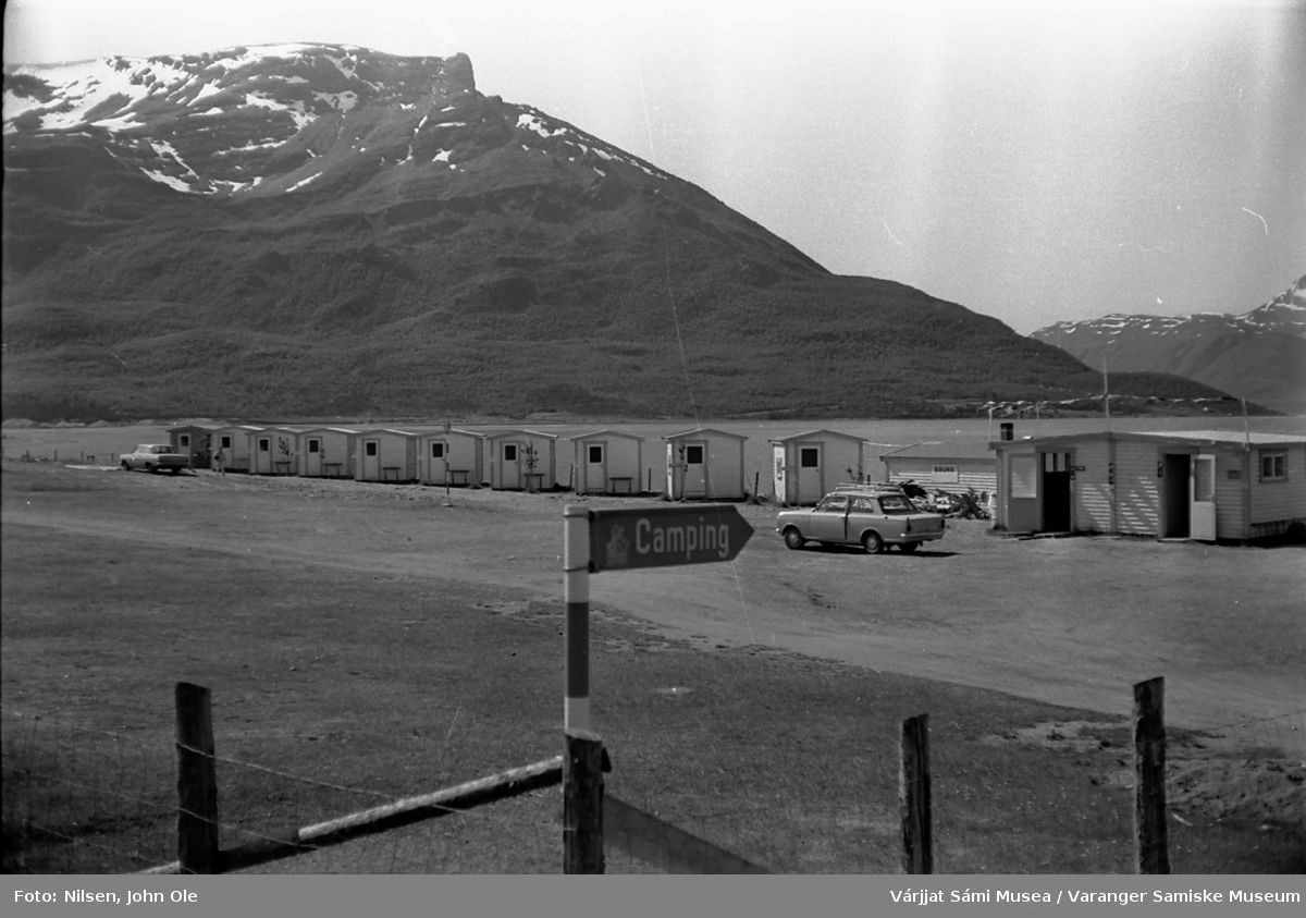 Campingplass i Skibotn området. Skilt i forgrunnen, hav og fjell med snødekt topp i bakgrunnen. 17. juli 1967