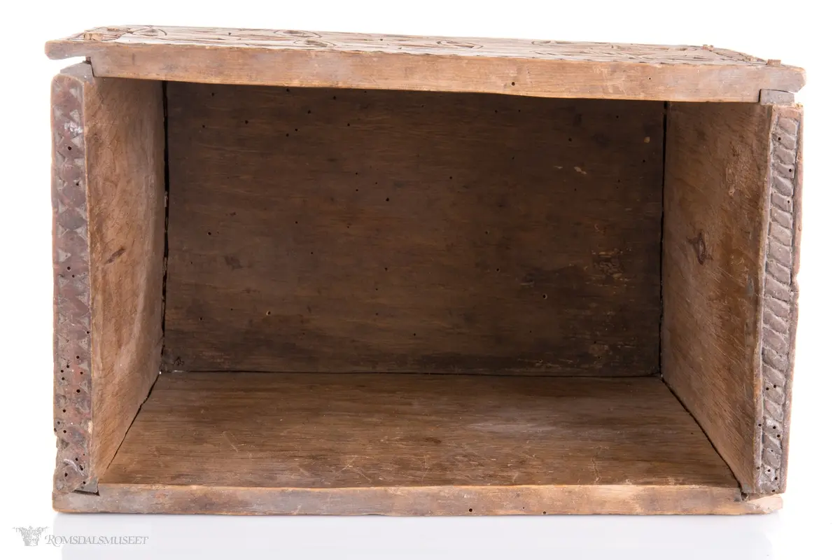 En stor og to små seksbladsroser i karveskurd på langsidene med skraverte dekorfelter og spetter rundt. På kortsidene er det skåret ut en stor seksbladsroser med rike dekorasjonsfelter bestående av spetter, streker diamantformer, sirkler med strek gjennom og solkors/kors. De største rosenen har kryss skåret inn på kronbladene.