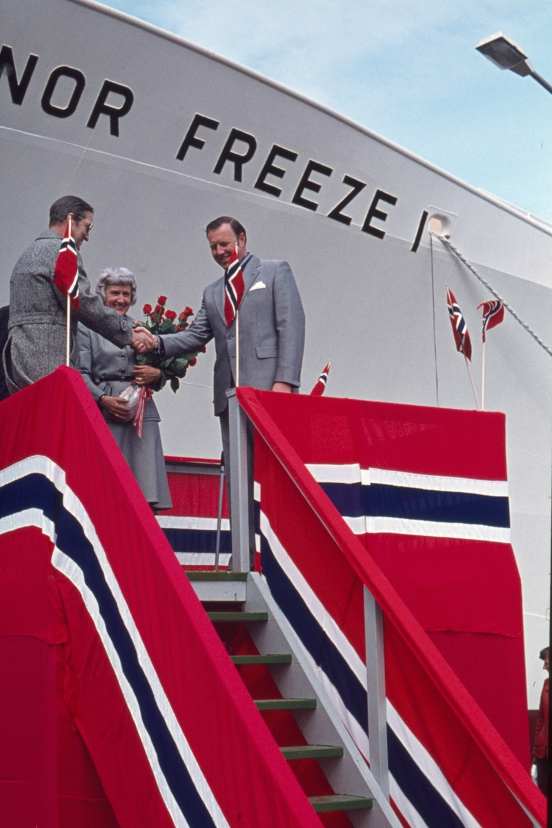 Erik Kaarbø og Per M. Hansen tar hverandre i handa på flaggdekket podium. "Nor Freeze I" og skipets gudmor i bakgrunnen.