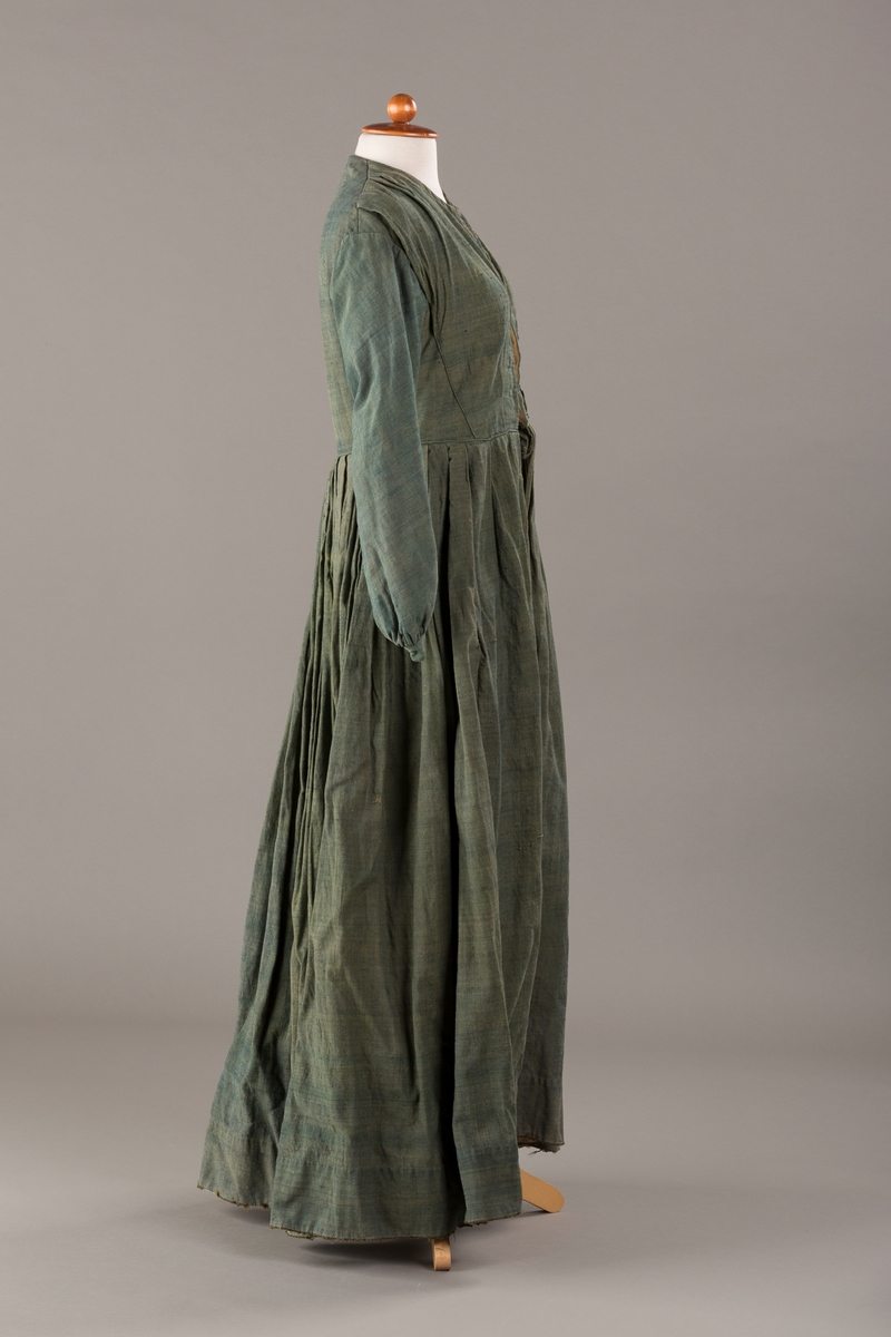 Form: Trangt liv med legg foran, skjørtet sydd med legg i livet.  God vidde i skjørtet, lange armer. Fem hekter i livet mangler.