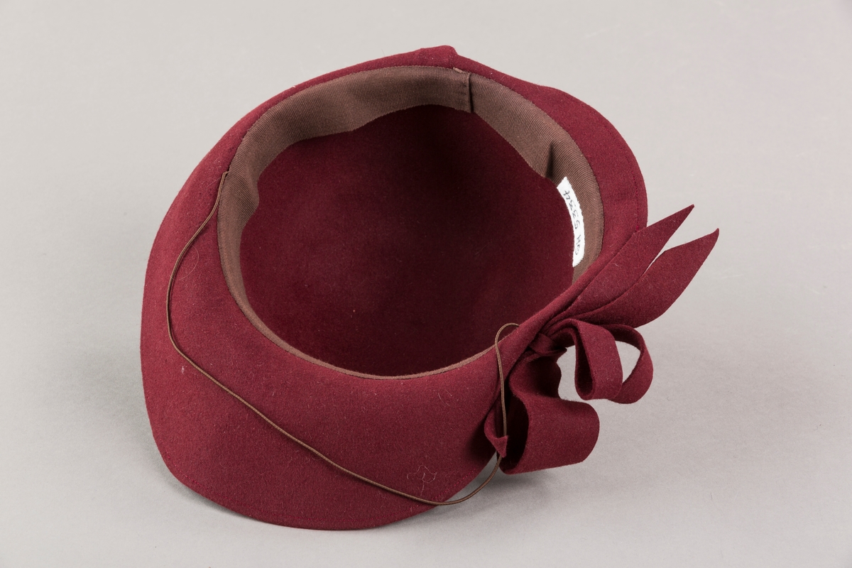 Form: Sirkelformet, avrundet  med asymetrisk brem og sløyfe. Bomullsbånd innvendig og hattestrikk