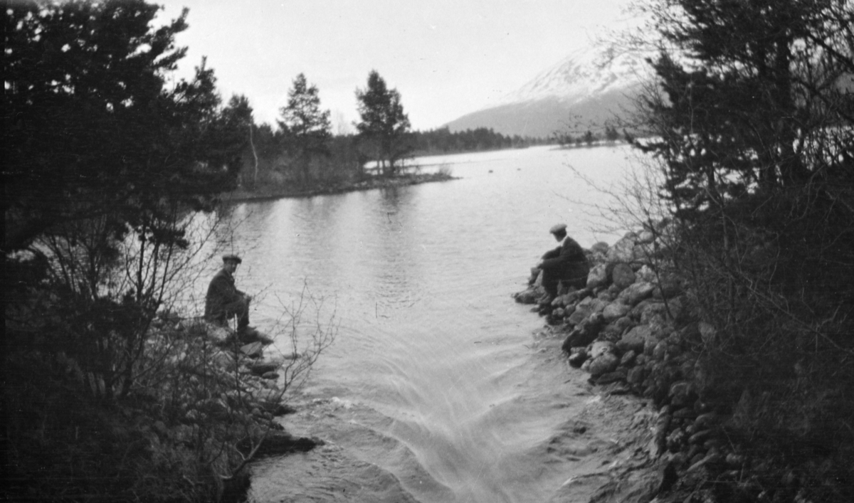 To menn sitter ved vann ved elveutgang.