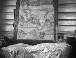 Innrammet bilde står på en divan støttet mot en tømmervegg. 