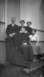 Mann og 4 kvinner på trappen ved hus.