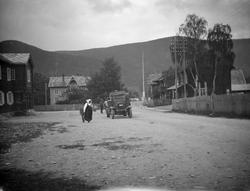 Veien i Vågåmo med bil, kvinne med bunad og et barn.