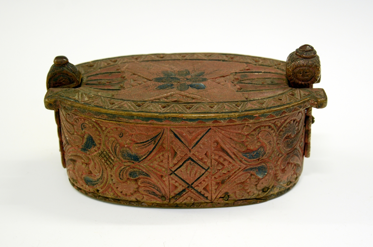 Tine av tre. Fra protokollen: Leikety-tine utskori i grovt kerbsnitt og plymrankkrullar. Under botnen skori 1814 og bokstavar. Standarane løglegt maksla som hovud med haarflettur. Raudmaala.