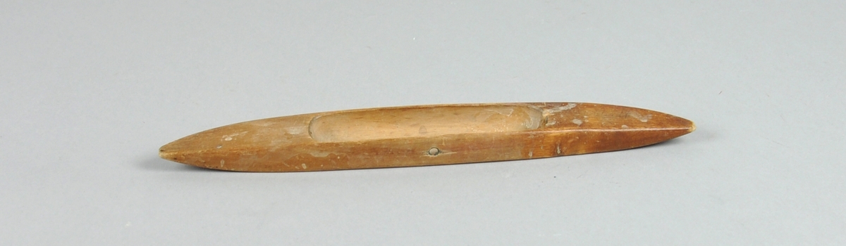 Avlang vevskyttel i tre, som er rett på den ene langsiden og buet på den andre. uthuling på midten.