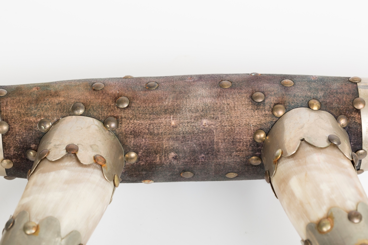 Knaggrekke antagelig håndlaget av kuhorn. 4 horn/kangger. Montert med "dekorative" beslag som er spikret og dekornaglet på hornene. Kledd med cordfløyelstoff på midtparti. To øyeskruer på toppen for feste til vegg.