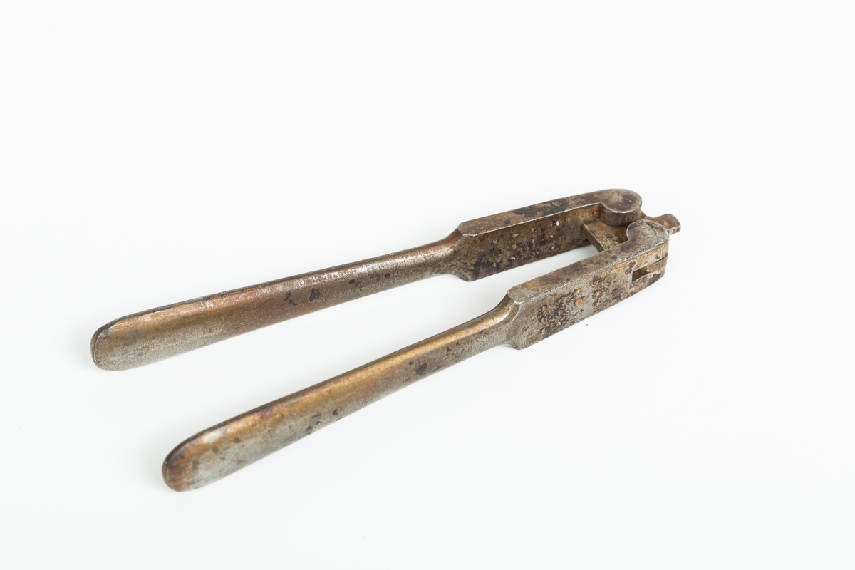 Nøteknekker i stål uten dekor. Utslåtte knaster på "gripeflatene". Hengsel med avstandstykker for to knekkeavstander.