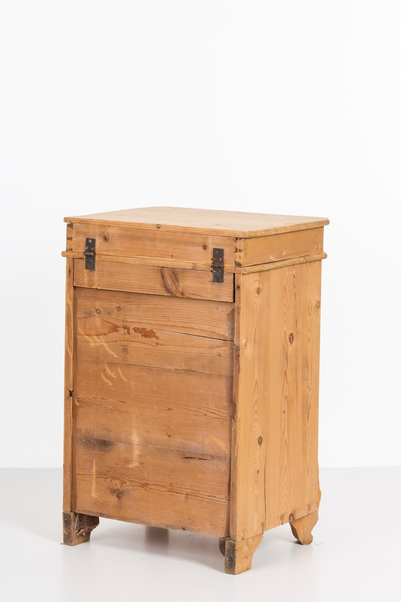 Toalettbord i ubehandlet tre. Det er rom for vaskebolle og skap under. Messingknott på døra til åpning og lukking, spor på innersiden av skapet kan tyde på at det tidligere også har vært en lås.