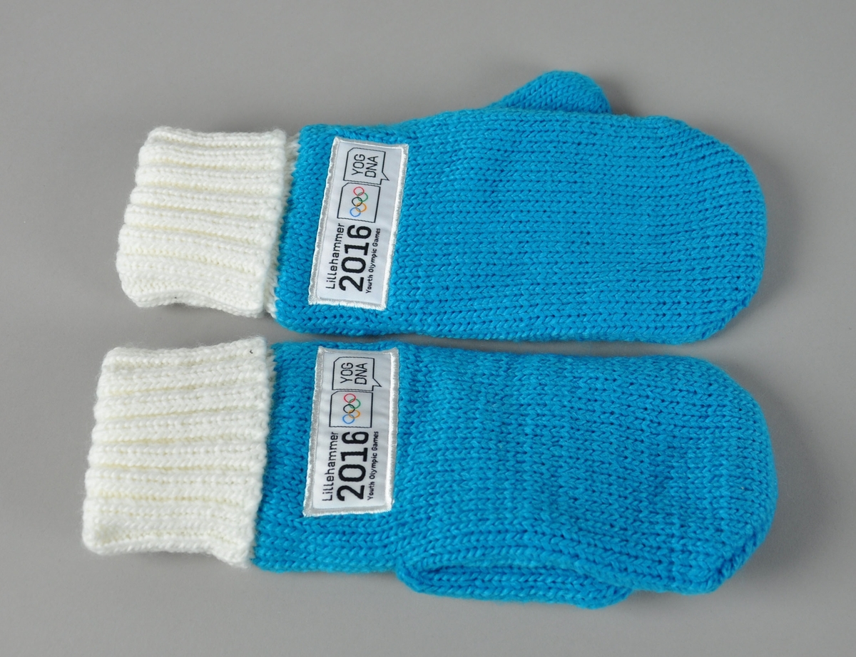 Ett par lyseblå strikkede votter med hvit vrangbord. Påsydd logo for Lillehammer Youth Olympic Games 2016.