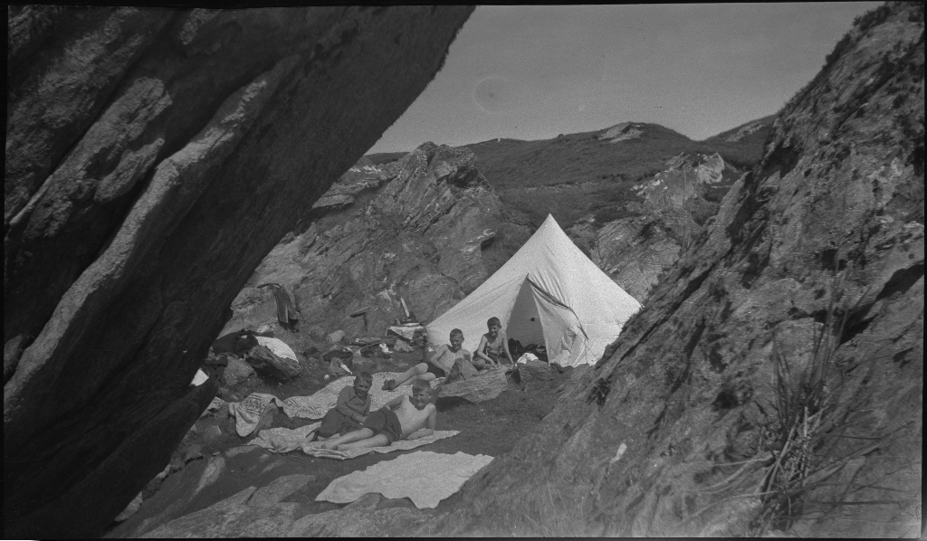 Barn og unge på og rundt stranda i Vigdelsvika. De fleste har satt opp telt, noen soler seg og noen bader. Den ene gutten på bilde nr. 6 holder et flytebelte.