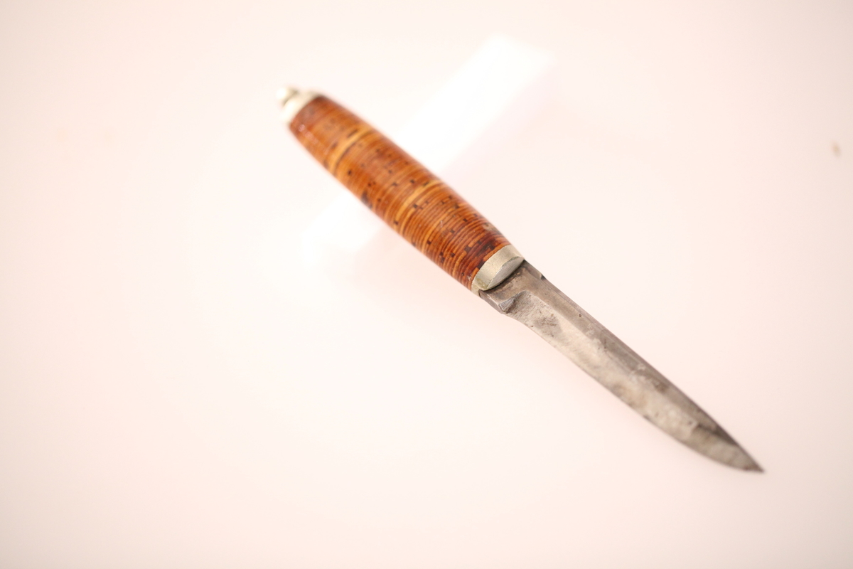 Kniv og slire hører ikke sammen. skaftet er laget av never, og slira er laget av nysølv. vanligvis hadde neverskaftkniver lærslire, og nysølvslirer hadde vanligvis ibenholdtskaft. Dekoren på slira er gravering og motivet er såkalte "Elstadkvister" slira er dermed høyest sannsynelig laget i Kolbu av en av Elstadkarene. Kniven har et fabrikkblad og er av ukjent opprinnelse.