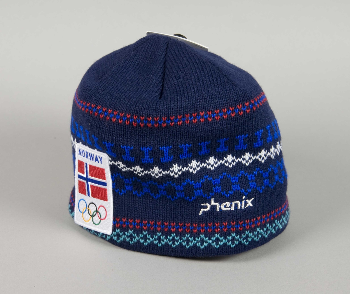 Blå lue med flerfarget mønster. Mønsteret består av horisontale rekker/linjer. På lua er det påsydd et merke med motiv av det norske flagget og de olympiske ringene.