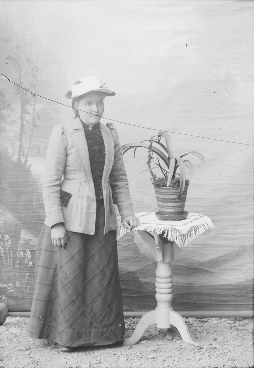 Kvinne står ved bord med blomst. Nevnt som Margit S. Jørstad